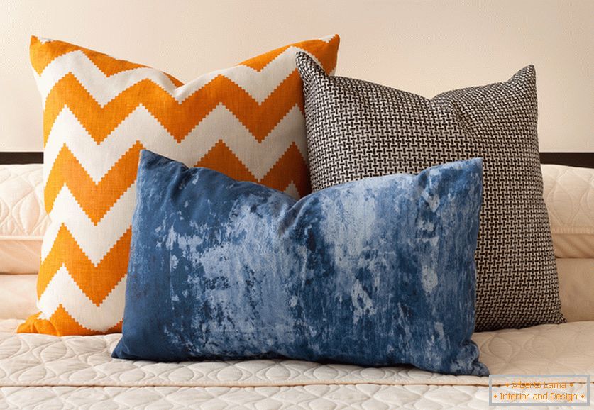 Svijetle narančaste, plave i crno-bijele ukrasne jastuke s zanimljivim ispisima na krevetu