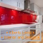 Bijeli namještaj i crvena pregača u unutrašnjosti kuhinje