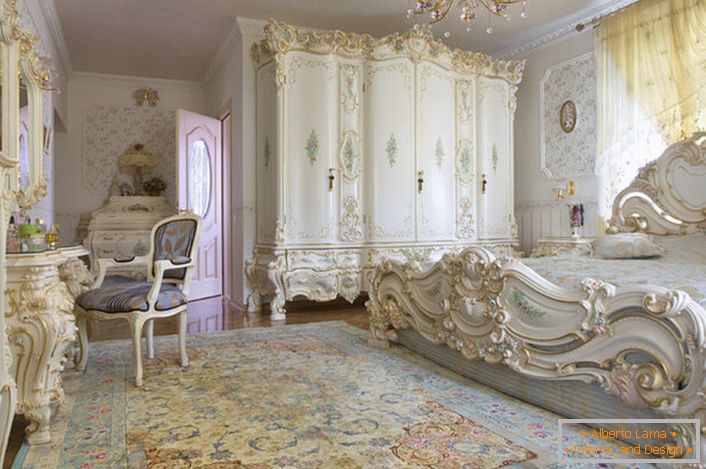 Sobno bijela spavaća soba s rezbarenim masivnim namještajem od drva. Krevet s visokom sjenicom na podu, elegantno se uklapa u unutrašnjost u baroknom stilu.