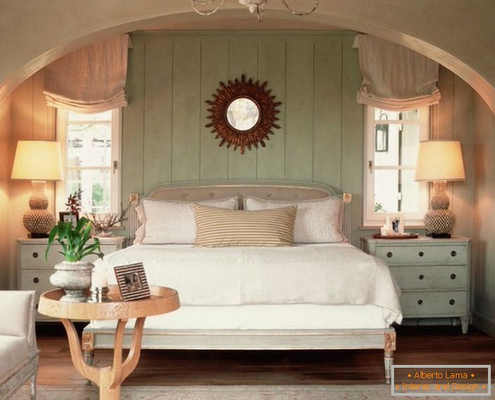 Obiteljska spavaća soba u seoskom stilu. Toplina doma, koliko je to moguće, naglašava mekani, volumetrijski krevet, prekriven jastucima.