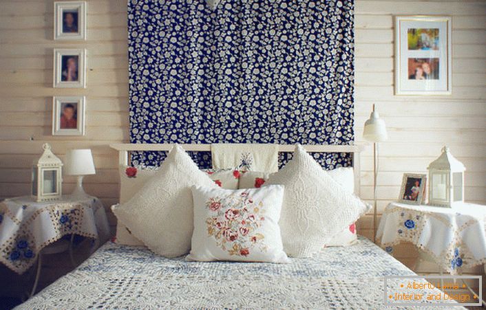 U skladu s rustikalnim stilom, krevet je ukrašen brojnim jastucima s kontrastnim crvenim vezom. Noćni stolovi prekriveni su stolnjakom s nježnim plavim cvjetovima.